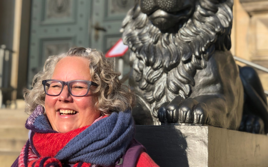 Meike Rensch-Bergner lächelnd in der Sonne vor dem Denkmal eines Löwens